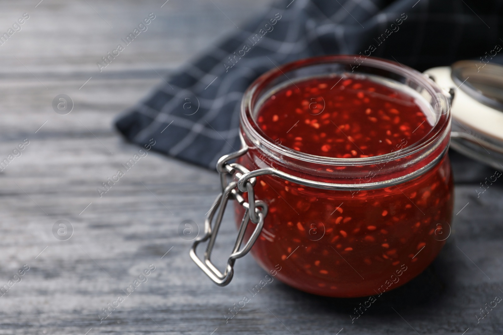 Photo of Homemade delicious raspberry jam on grey wooden table. Space for text