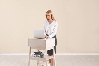 Young woman using laptop at stand up workplace against light wall