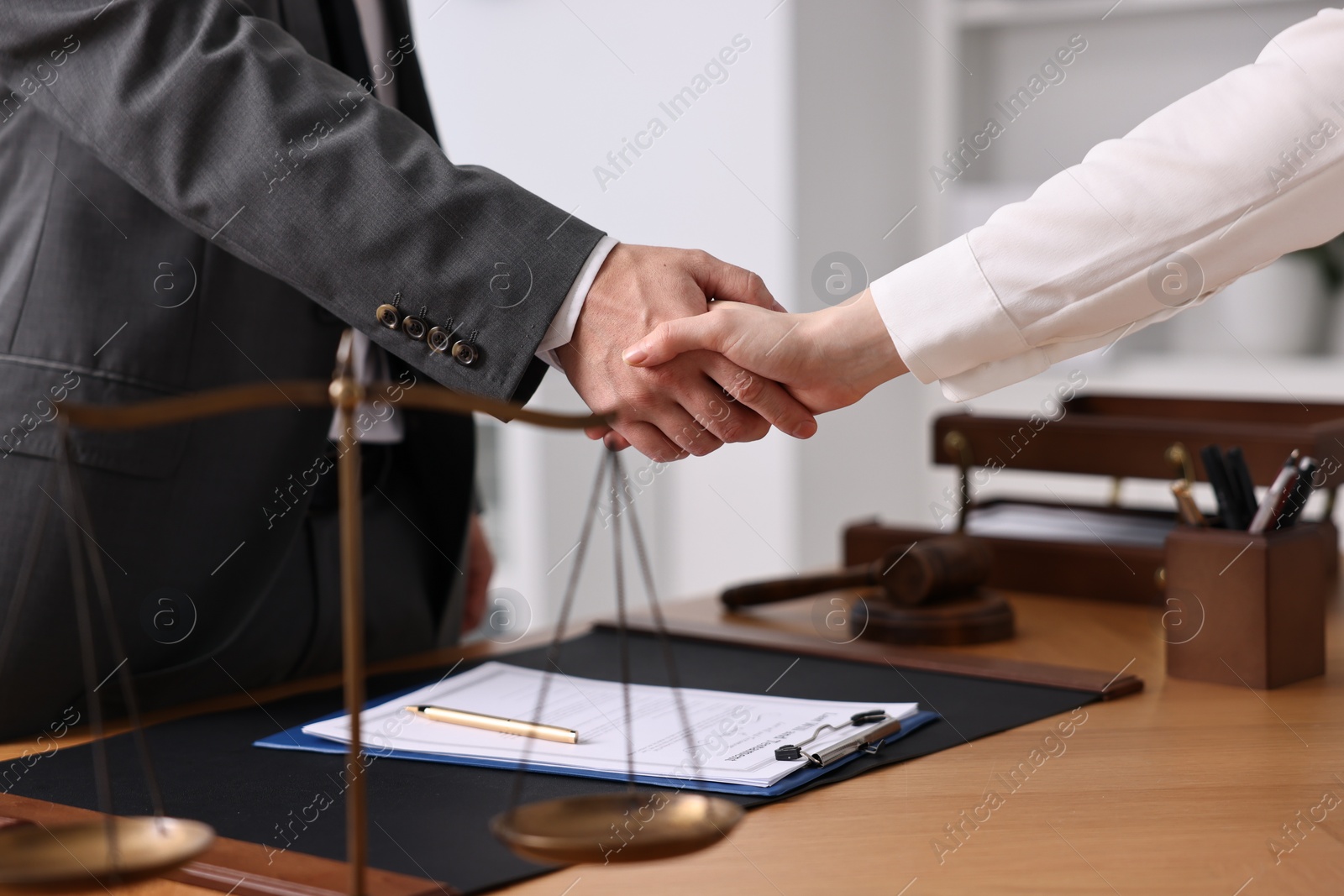 Photo of Notary shaking hands with client at wooden table in office, closeup