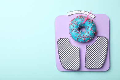 Photo of Scales made with donut and paper on light blue background, top view. Space for text