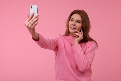 Beautiful woman taking selfie on pink background