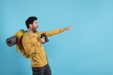 Photo of Emotional man with backpack and binoculars on light blue background, space for text. Active tourism
