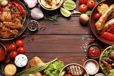 Flat lay composition with delicious barbecued meat and vegetables on wooden background. Space for text