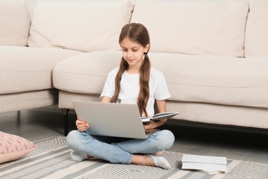 Girl with laptop and books sitting on floor at home