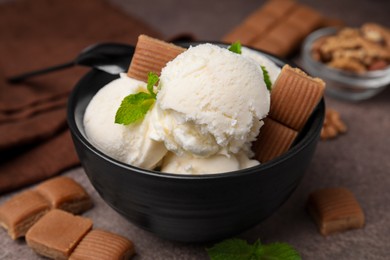 Tasty ice cream with caramel candies and mint in bowl on brown table, closeup