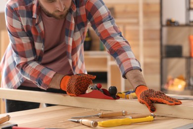 Carpenter shaping wooden bar with hand plane at table in workshop, closeup