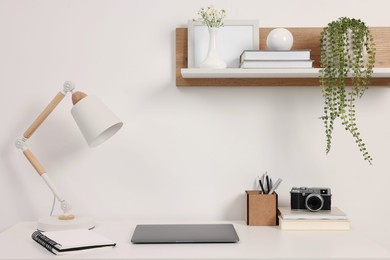 Photo of Home office. Laptop, vintage camera, lamp and stationery on white desk indoors