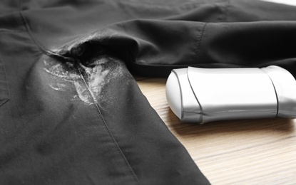 Photo of Black shirt with stain and deodorant on wooden background, closeup