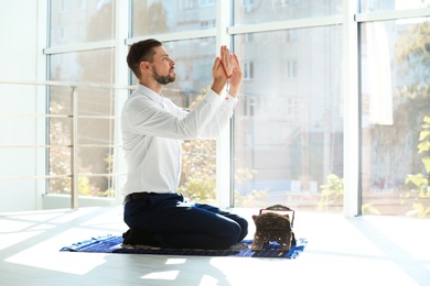 Photo of Muslim man in suit praying on rug indoors