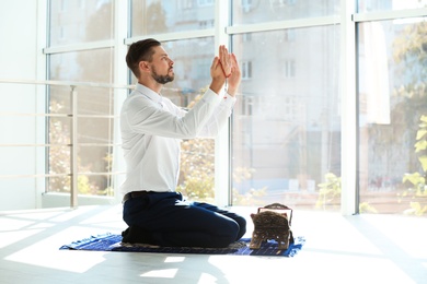 Muslim man in suit praying on rug indoors