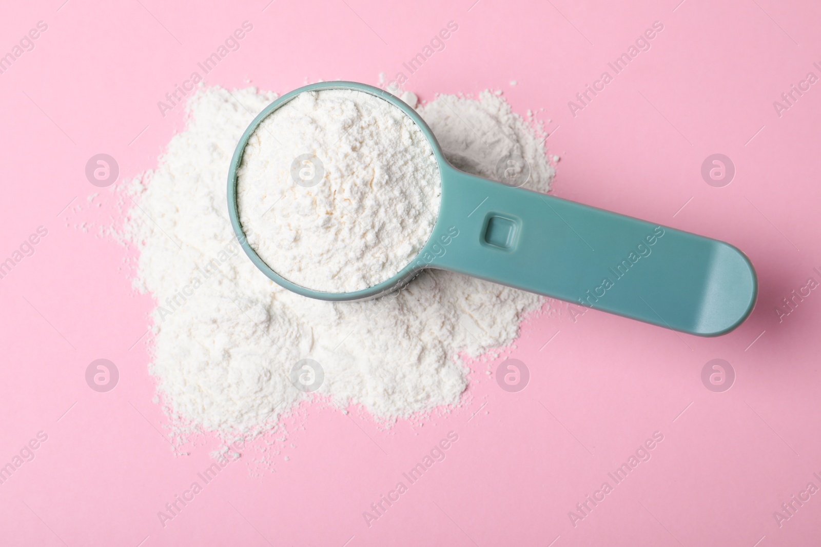 Photo of Scoop and pile of protein powder on pink background, flat lay