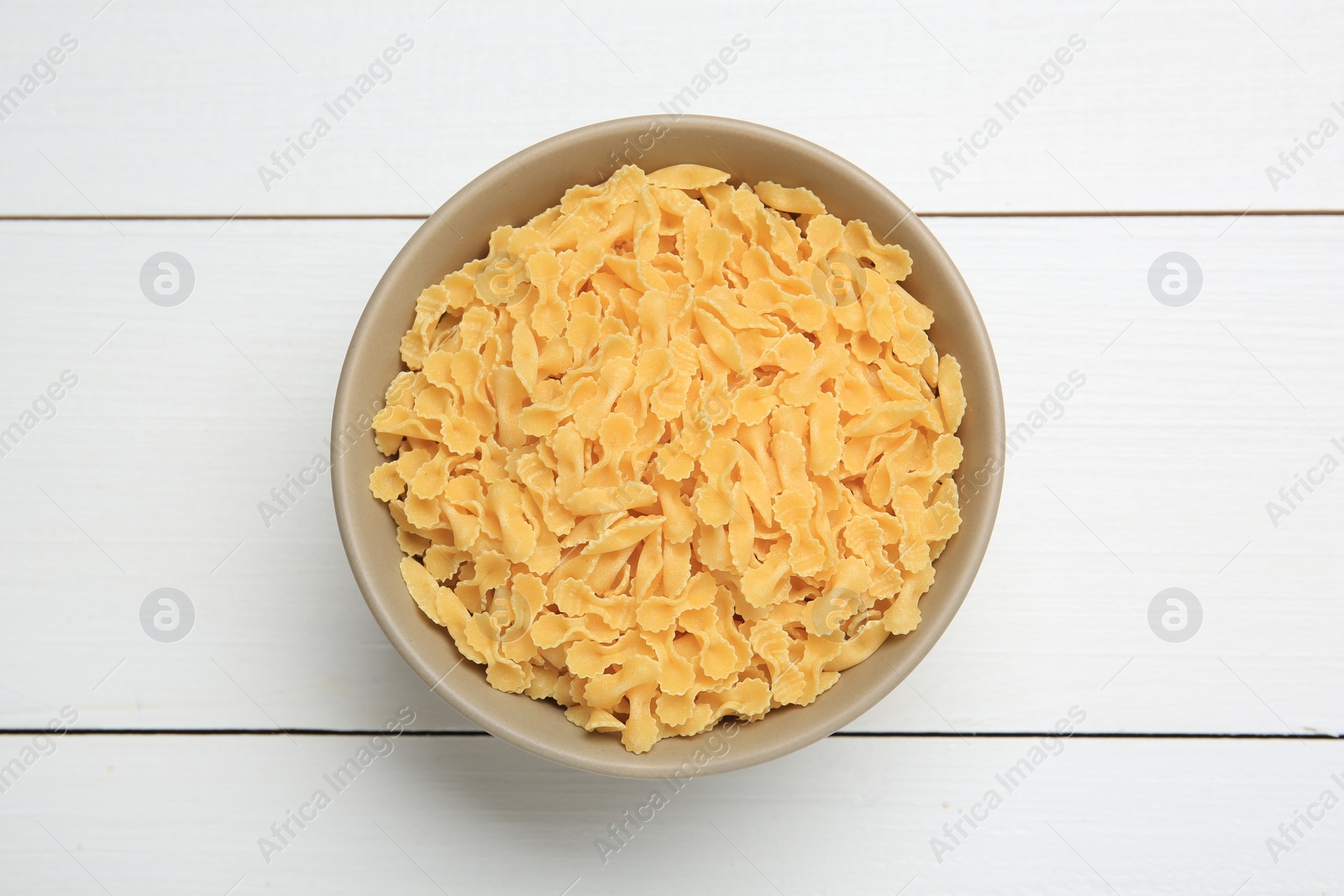 Photo of Raw farfalline pasta in bowl on white wooden table, top view