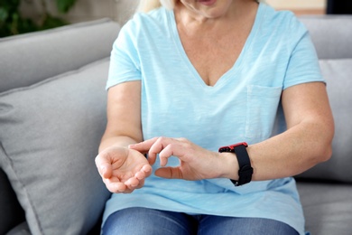 Mature woman checking pulse with fingers at home, closeup