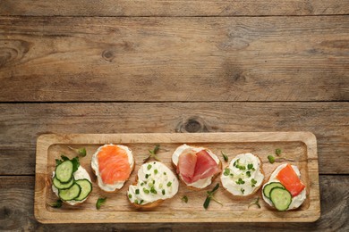 Delicious sandwiches with cream cheese and other ingredients on wooden table, top view. Space for text