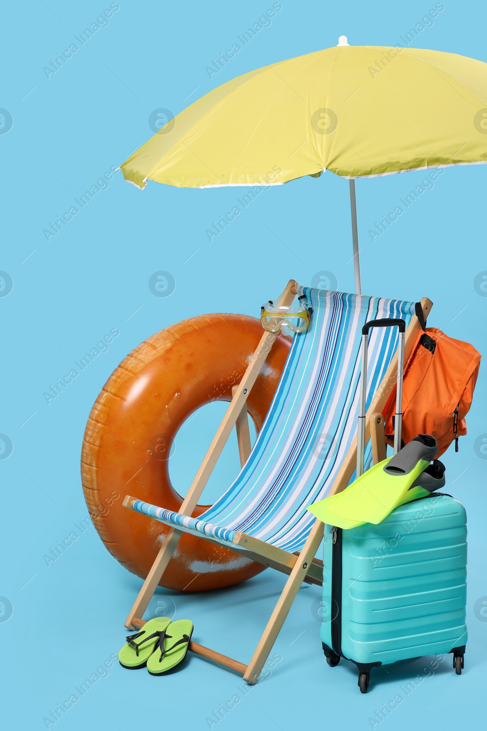 Photo of Deck chair, suitcase, backpack and beach accessories on light blue background