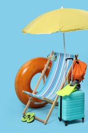 Photo of Deck chair, suitcase, backpack and beach accessories on light blue background