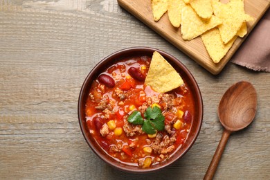 Tasty chili con carne with nachos served on wooden table, flat lay