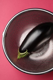 Photo of Colander with fresh eggplant on pink table, top view