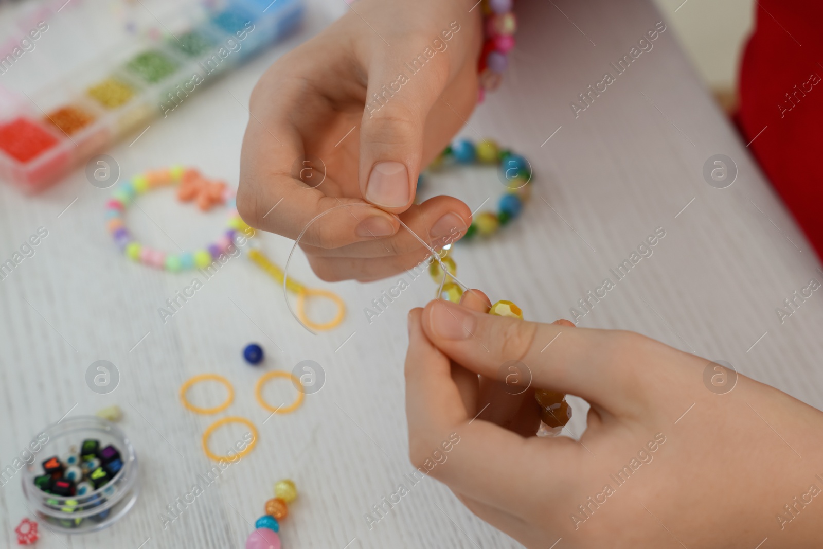 Photo of Girl making beaded jewelry at white wooden table, closeup