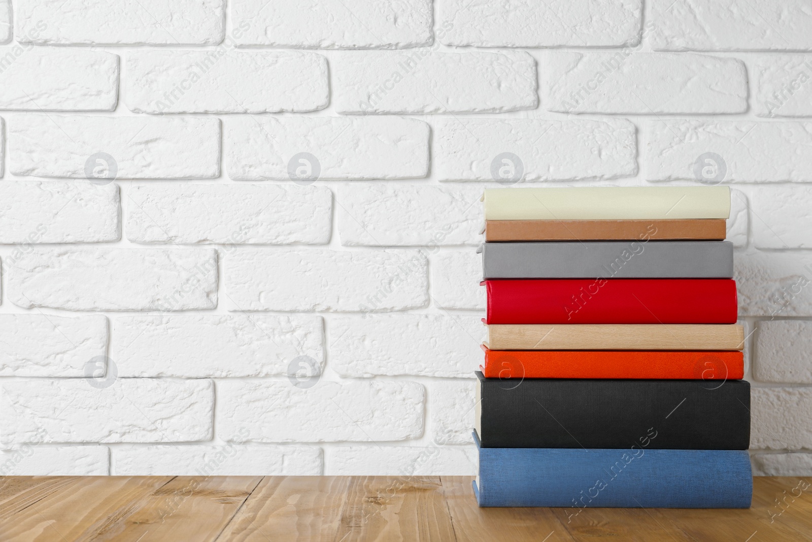 Photo of Books on wooden table near white brick wall, space for text