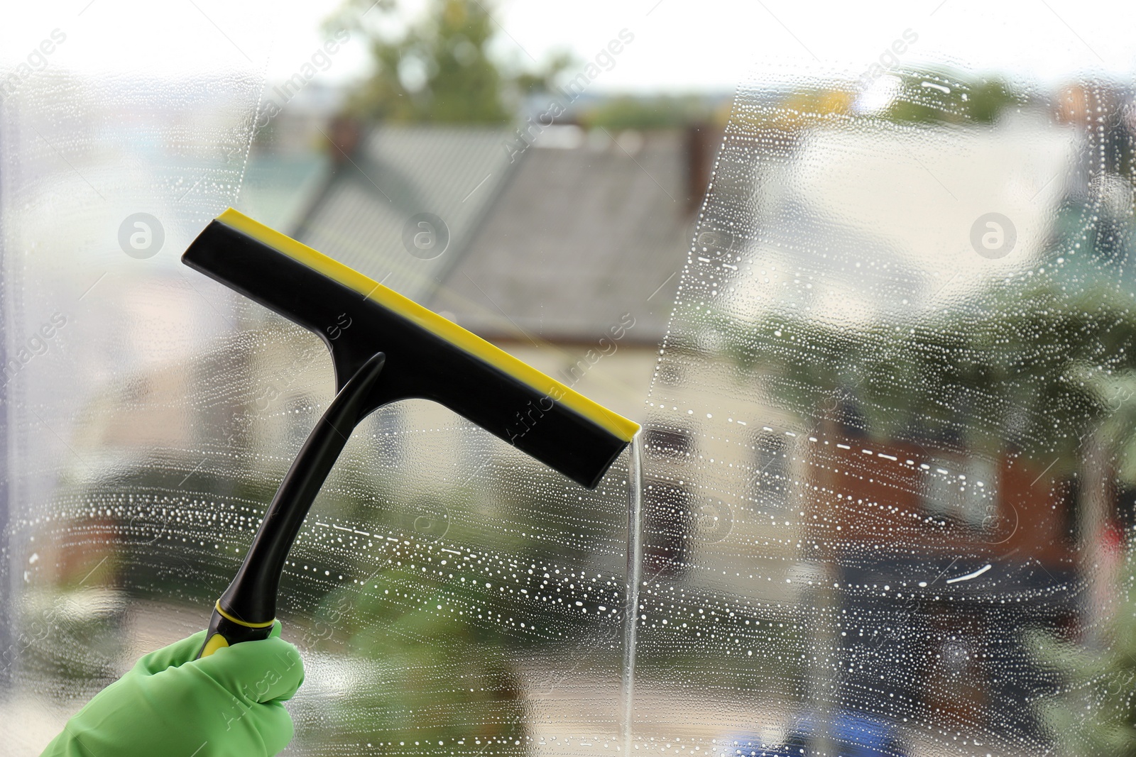 Photo of Woman cleaning glass with squeegee indoors, closeup