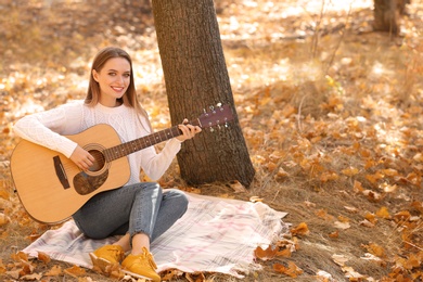 Teen girl playing guitar in autumn park