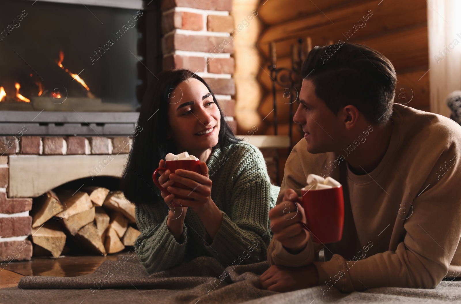 Photo of Lovely couple with delicious cocoa near fireplace on floor at home. Winter vacation