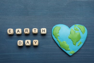 Photo of Cubes with words Earth Day and heart shaped plasticine planet on blue wooden table, flat lay