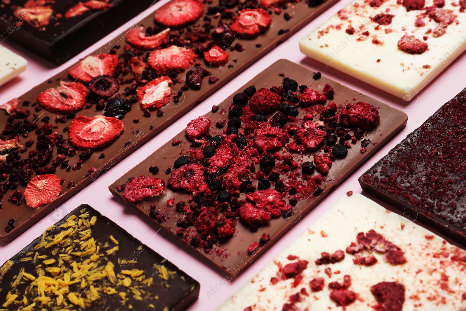 Photo of Different chocolate bars with freeze dried fruits on pink background