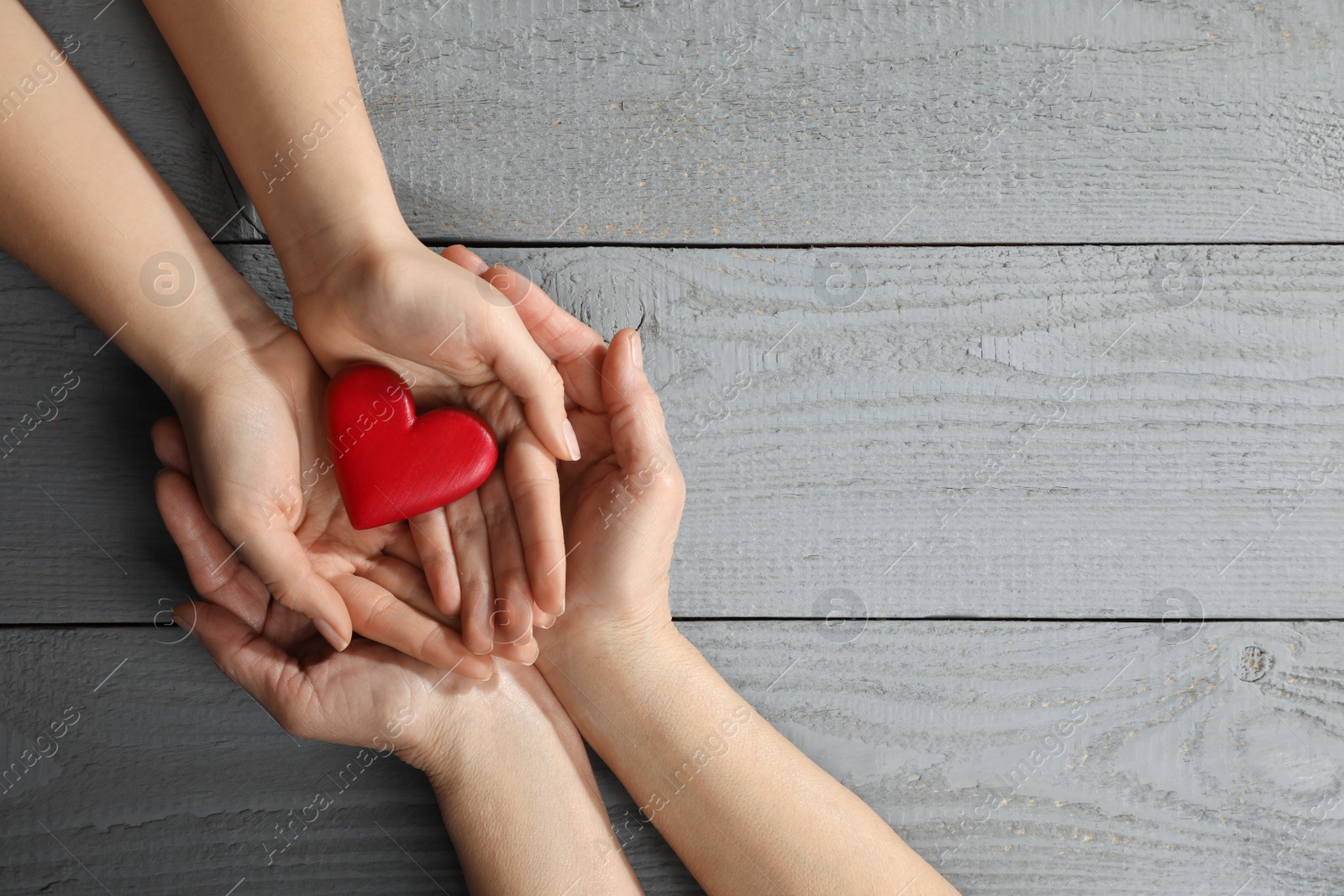 Photo of Young and elderly women holding red heart at grey wooden table, top view. Space for text