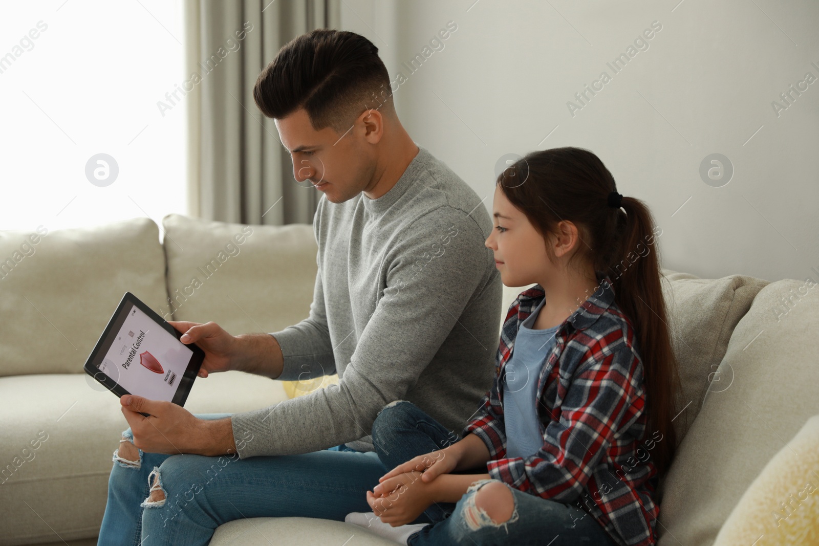 Photo of Father installing parental control app on tablet to ensure his child's safety at home