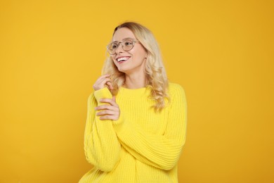 Photo of Happy woman in stylish warm sweater and eyeglasses on orange background