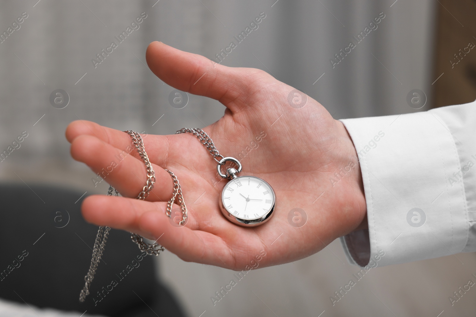 Photo of Man holding chain with elegant pocket watch on blurred background, closeup