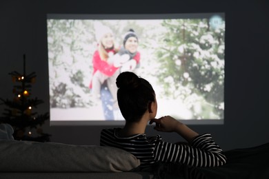 Photo of Woman watching romantic Christmas movie via video projector at home, back view