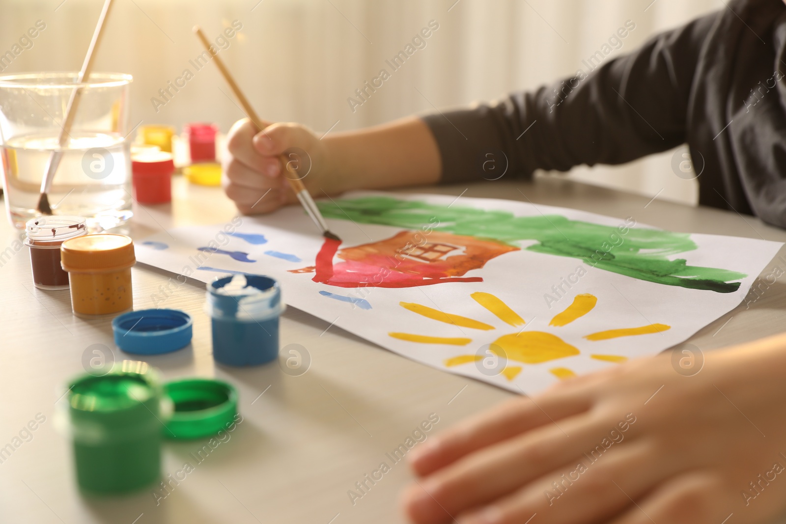 Photo of Little boy drawing picture with brush at wooden table indoors, closeup. Child`s art