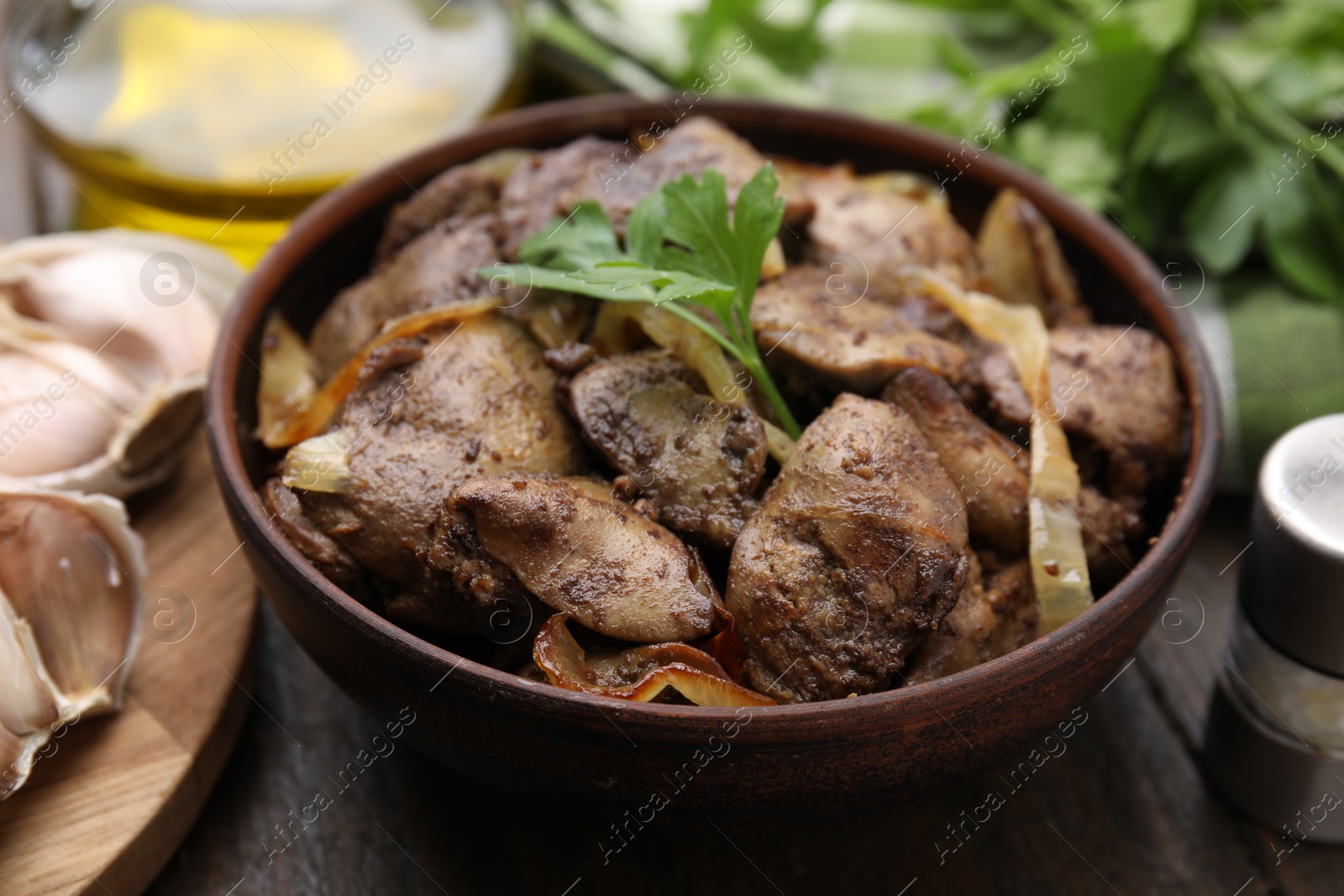 Photo of Tasty fried chicken liver with onion and parsley in bowl on wooden table, closeup