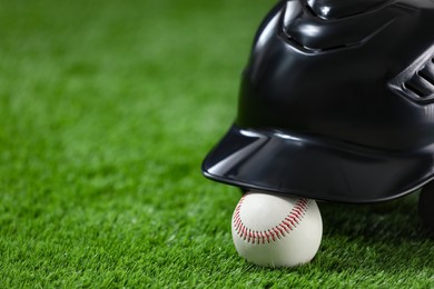 Photo of Batting helmet and baseball ball on green grass, closeup. Space for text