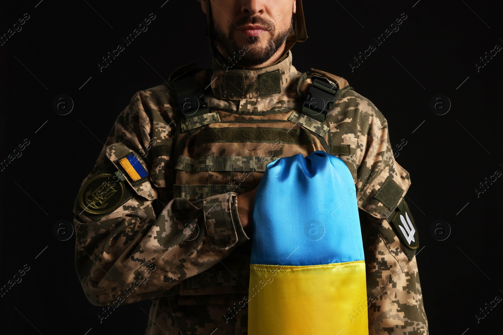 Photo of Soldier in military uniform with Ukrainian flag on black background, closeup