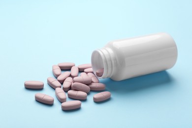 Vitamin pills and bottle on light blue background, closeup