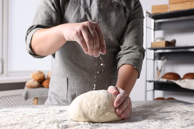 Man sprinkling flour over dough at table in kitchen, closeup