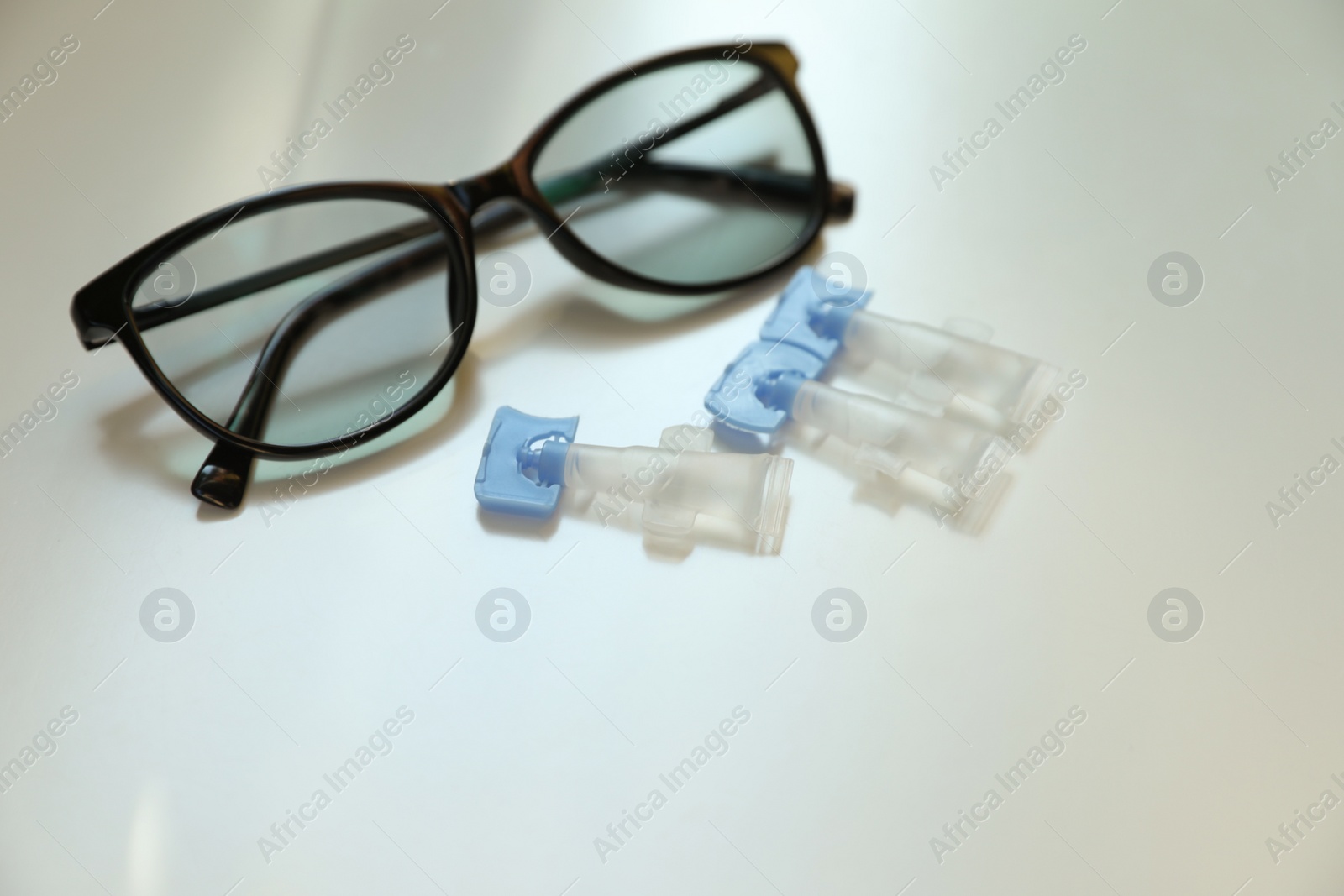 Photo of Single dose eye drops and glasses on white table