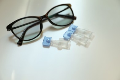 Single dose eye drops and glasses on white table