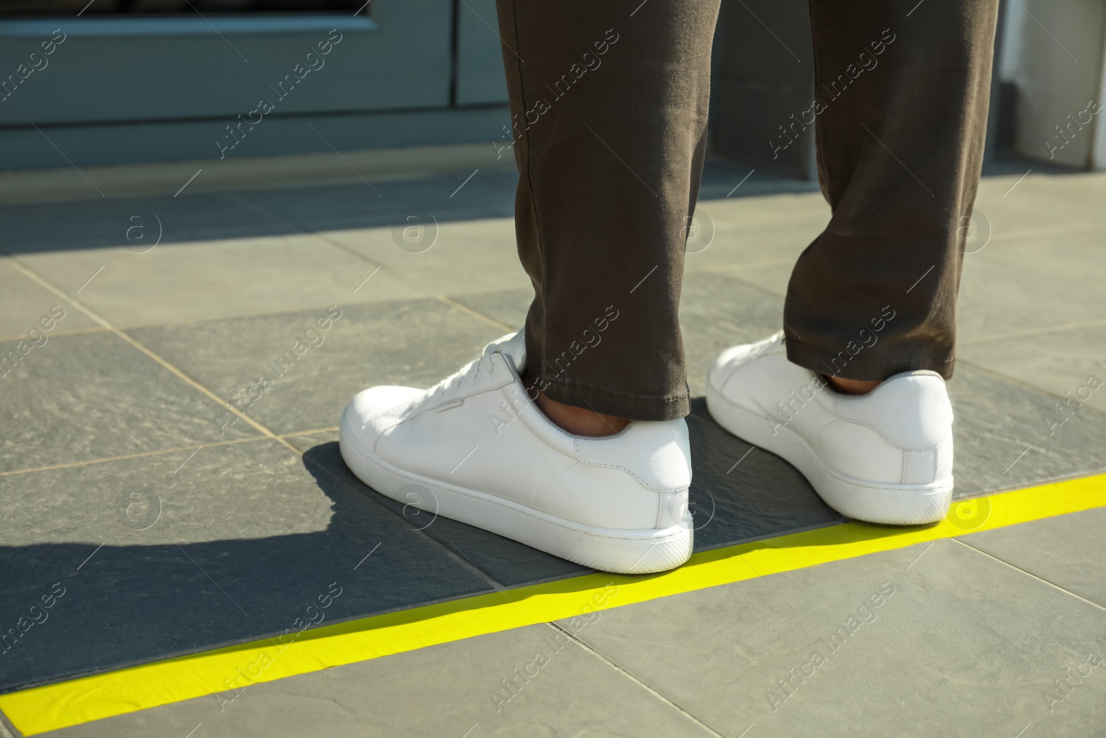 Photo of Man standing on taped floor marking for social distance outdoors, closeup. Coronavirus pandemic