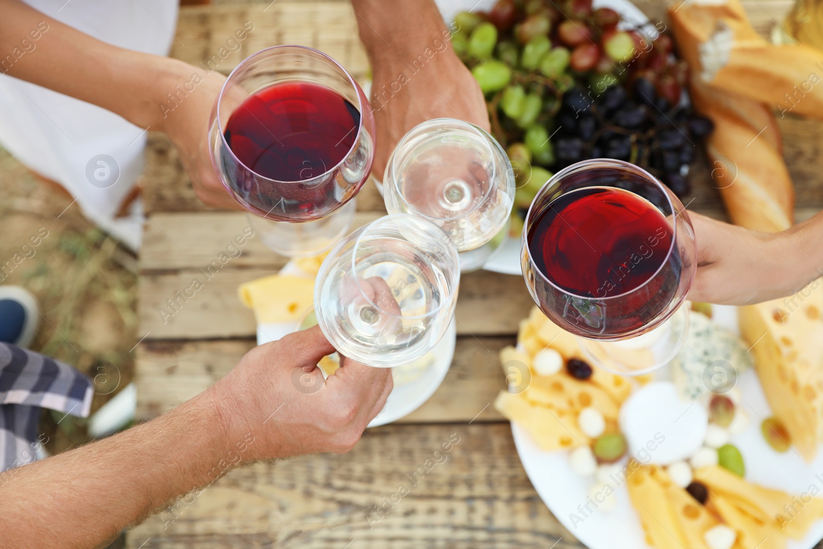 Photo of Friends holding glasses of wine over picnic table at vineyard, top view