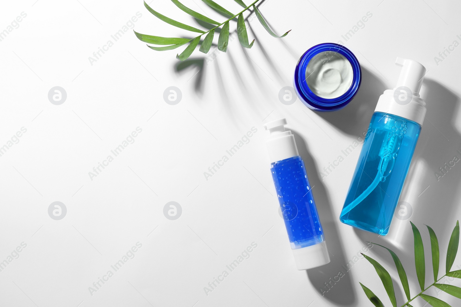 Photo of Set of cosmetic products and green leaves on white background, flat lay. Space for text