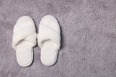 Photo of Soft white slippers on fluffy grey carpet, top view. Space for text