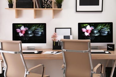 Photo of Modern workplace with large desk and computers in room. Stylish interior