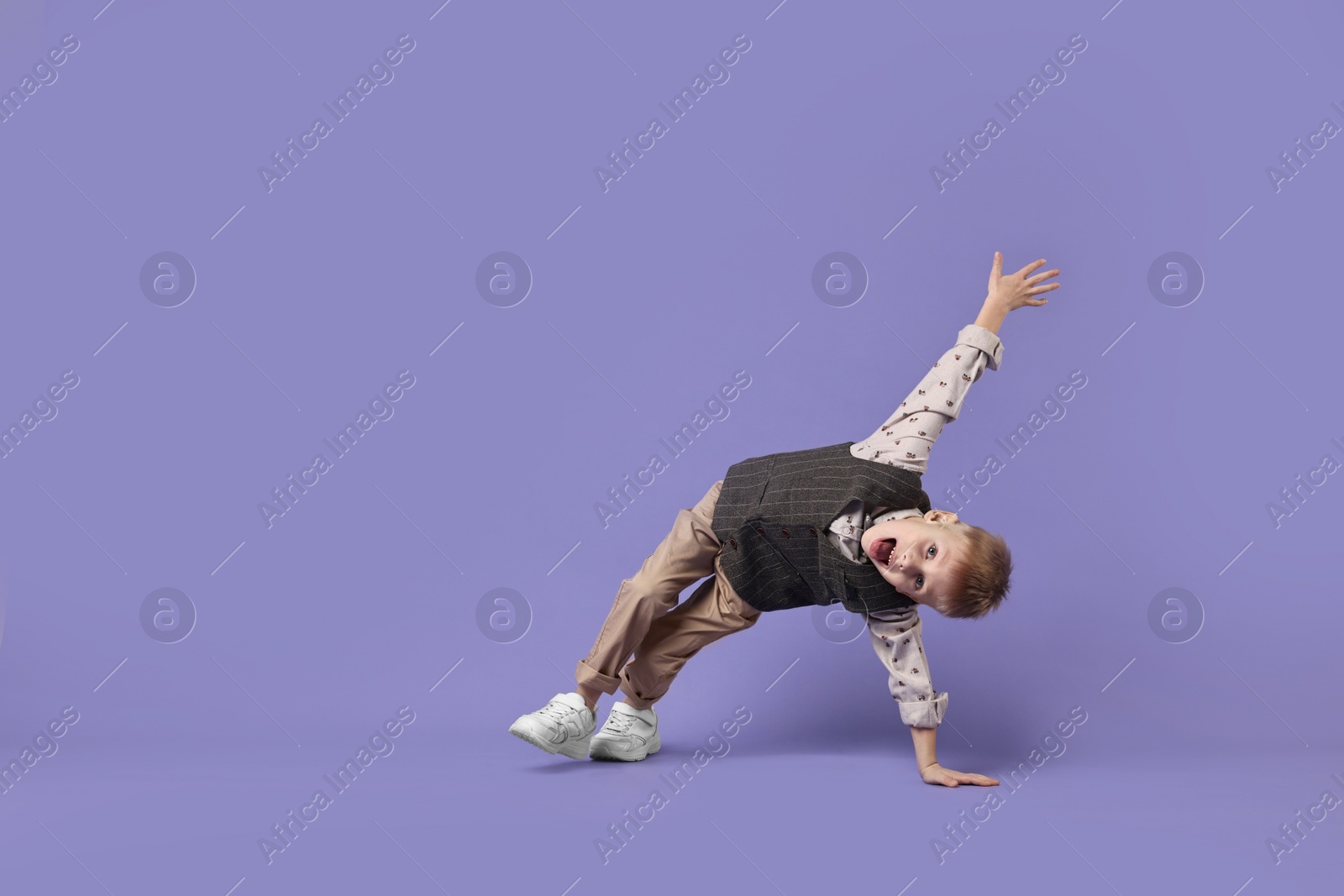 Photo of Happy little boy dancing on violet background. Space for text