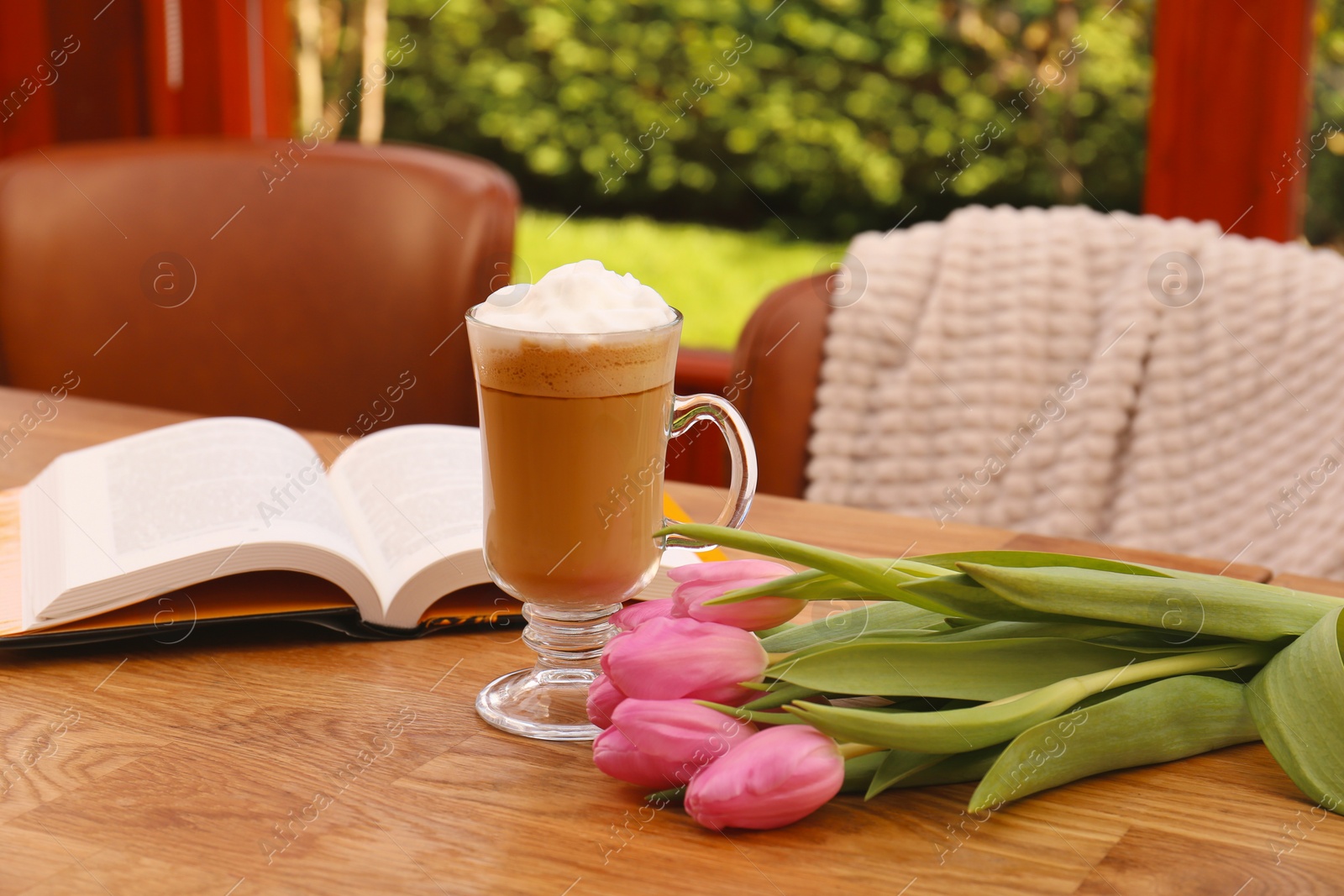 Photo of Glass of delicious cocoa, pink tulips and book on wooden table at terrace