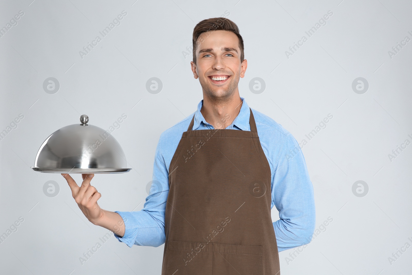 Photo of Handsome waiter holding metal tray with lid on light background